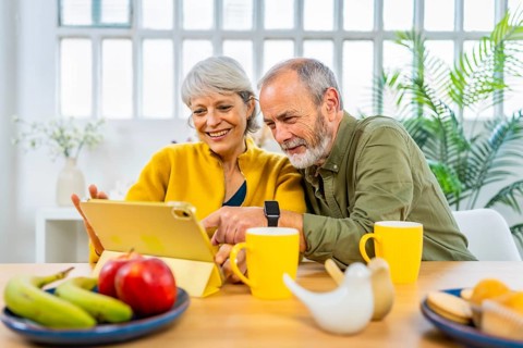 Happy caucasian modern senior couple surfing the net using digital tablet at home