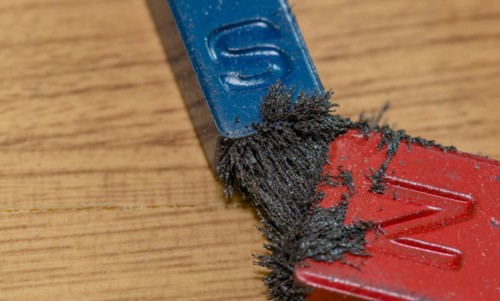 Closeup of iron filings attached to both the north and south end of colored magnets on wood grain