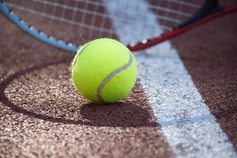 Shadows of racquet surrounding a tennis ball near white line on outdoor court in sunshine, sport