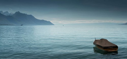 A beautiful view of Lake Geneva and surrounding mountains on a summer day with a single boat in the