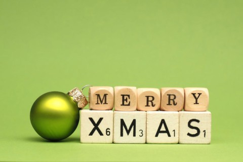 Wooden blocks with the words Merry Christmas and a Christmas bauble on a green background, space