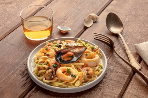 Seafood pasta. Tagliolini with mussels, shrimps, clams and squid rings, with a glass of wine on a