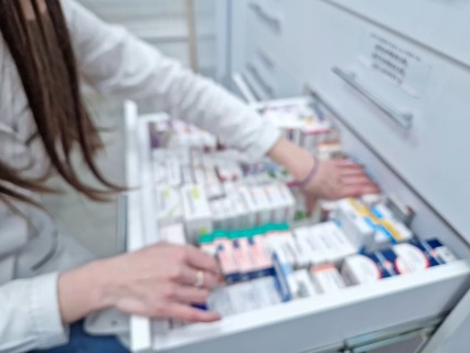 Defocused view inside of pharmacy with female pharmacist stores the medicine inside the drawers and