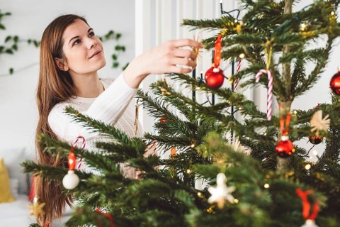 Beautiful smiling cheerful caucasian woman dressed in white outfit decorating a natural Christmas