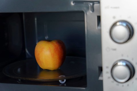 A fresh red apple placed inside a microwave oven