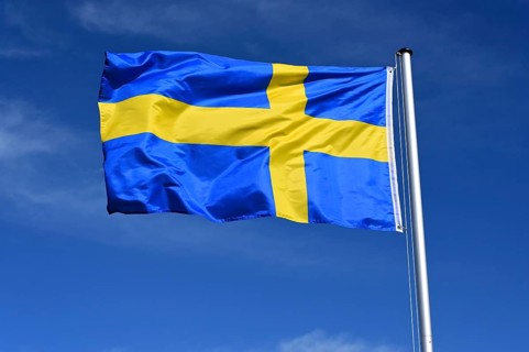 The flag of Sweden flutters in the wind against a blue cloudless sky