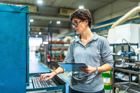 Female adult manager of a factory using computer while checking the quality of products and doing