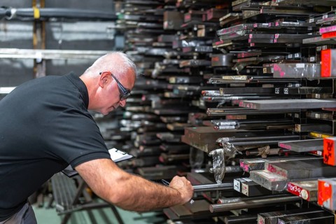 Mature caucasian male inspector doing inventory and measuring metal bars in a factory
