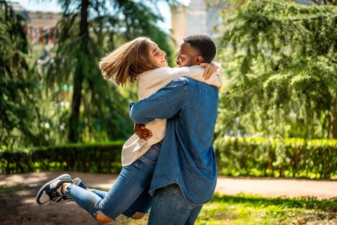 Caucasian woman jumping to hug her african male partner in a park
