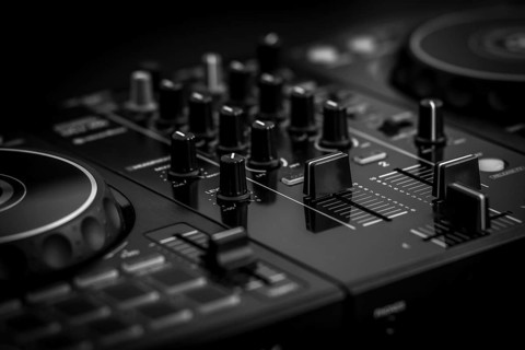 Close-up of a black DJ mixer featuring numerous knobs and faders, captured in a monochrome setting,