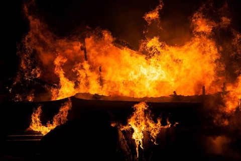 Arson or nature disaster, burning fire flame on wooden house roof