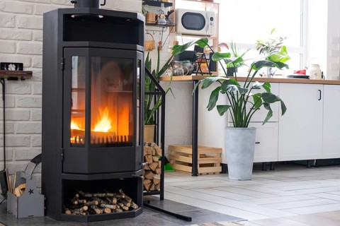 Black Metal Steel fireplace stove with fire and firewood near kitchen in village house. Cozy home