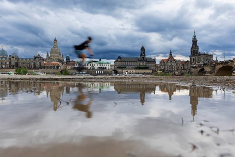 The Dresden silhouette with a cyclist and dark clouds behind the Church of Our Lady is reflected in