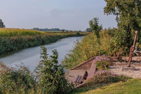 A quiet river flows along a bank with benches, flowers and trees, krummhörn, east frisia, germany