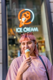 Vertical photo of a modern girl with pink colored hair eating ice cream outside the store