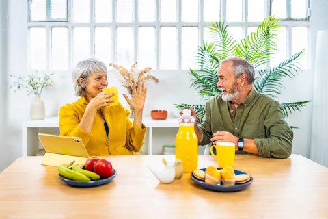 Frontal view of a happy caucasian mature couple talking while eating healthy breakfast at home