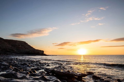 View of the sunrise over the Atlantic. View over a stone beach on a volcanic island. Cold lava