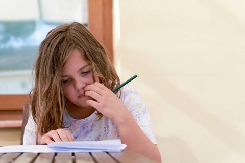 Close-up of a beautiful blonde girl in a colorful dress concentrating on school homework