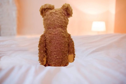 Teddy bear sitting on a bed, symbolic image Lonely childhood