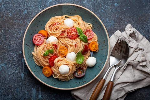 Delicious spaghetti with mozzarella, colourful cherry tomatoes, fresh basil on ceramic plate on