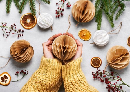 Hands holding a beige paper ball surrounded by Christmas decorations on a table. Handmade honeycomb