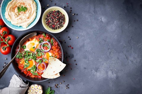 Shakshuka with pita bread in pan, hummus in bowl on rustic background. Middle eastern traditional