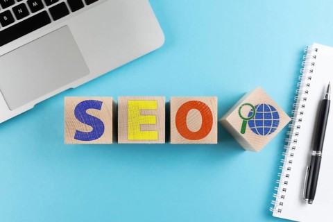 top view of letters SEO and internet search symbol on wooden cubes on blue background with laptop