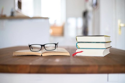 Stack of books and glasses lying on wooden desk at home. Knowledge and science