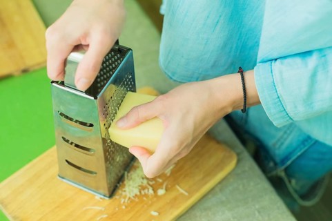 Close-up of a woman's hands rub a parmesan cheese on a metal grater on a green table