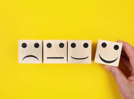 directly above view of smiley feedback icons on wooden blocks against yellow background