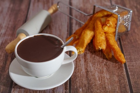 White cup of hot chocolate with churros typical spanish breakfast on a wooden table
