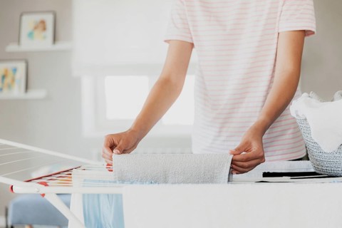 Woman hanging clean wet clothes laundry on drying rack at home in room. Detail of female housewife