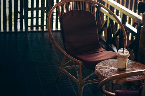 Rattan chair with a brown cushion beside a small circle table holding an iced coffee on a cozy