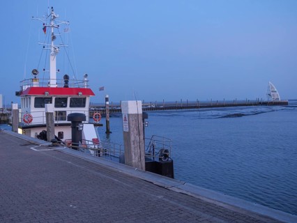 A ship lies at the dock of a harbour at dusk, the calm waters reflect the evening light, juist,