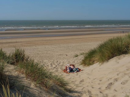Person relaxing on a blanket in a sand dune on the beach, overlooking the calm sea, de haan,
