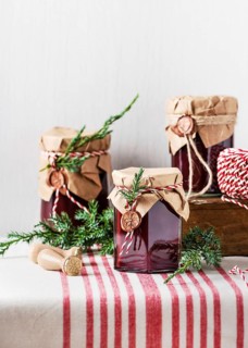 Preserving jars with red jams, decorated with fir branches and paper, arranged on a striped cloth,