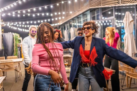 Happy multi-ethnic women dancing together at the terrace of a night bar