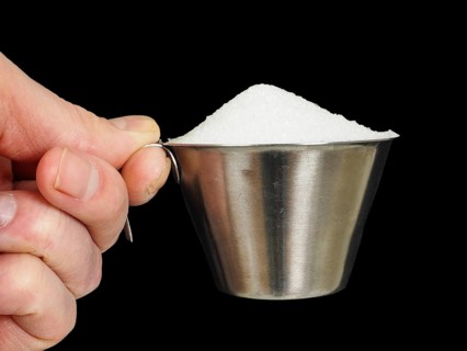 Person holding a measuring cup of one deciliter filled up with white granulated sugar, isolated on
