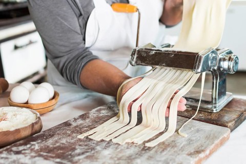 Baker cutting raw dough into tagliatelle pasta machine wooden board