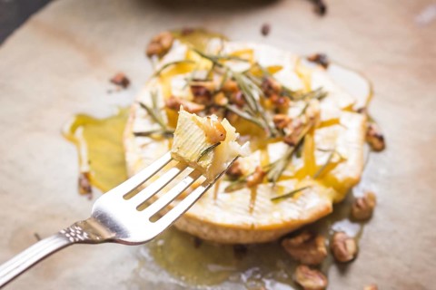 Piece of baked camambert on a fork. Delicious baked cheese with honey, walnuts, herbs and pears