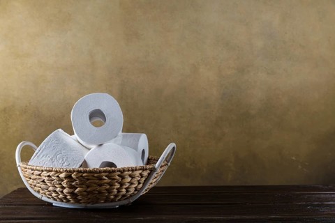 Rolls of toilet paper in the basket on the wooden background