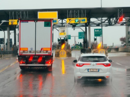 Car waiting at a toll booth with traffic lights and payment lanes on a rainy day, A1 A8 highway