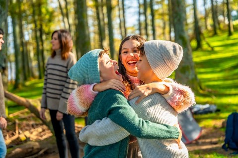 Brothers hugging enjoying camping day with family while parents talking on the background in an