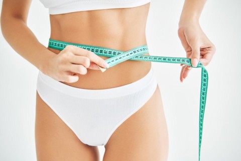 Young slim woman measuring her waist by measure tape on white background. Healthy lifestyle, diet
