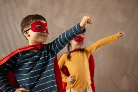 Portrait of a team of two young superheroes, brother and sister, over beige background. Superhero