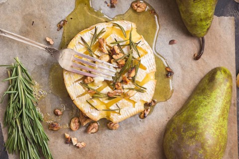 Delicious beautiful baked camembert with fork. Cheese with honey, walnuts, herbs and pears
