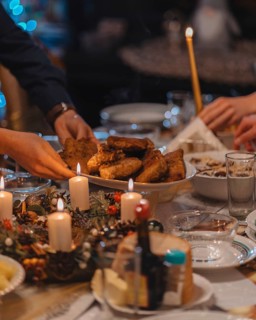Christmas Supper. People serving dishes to each other. On the set table fish, candles, wreath. A