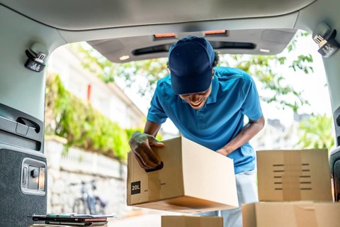 Delivery african man with blue uniform and cap working with several packages on van