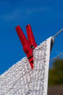 Red clothes peg holding a wet towel on a clothesline, in front of a blue sky, Weseke, Münsterland,