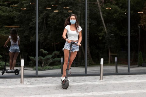 Woman with mask riding electric scooter